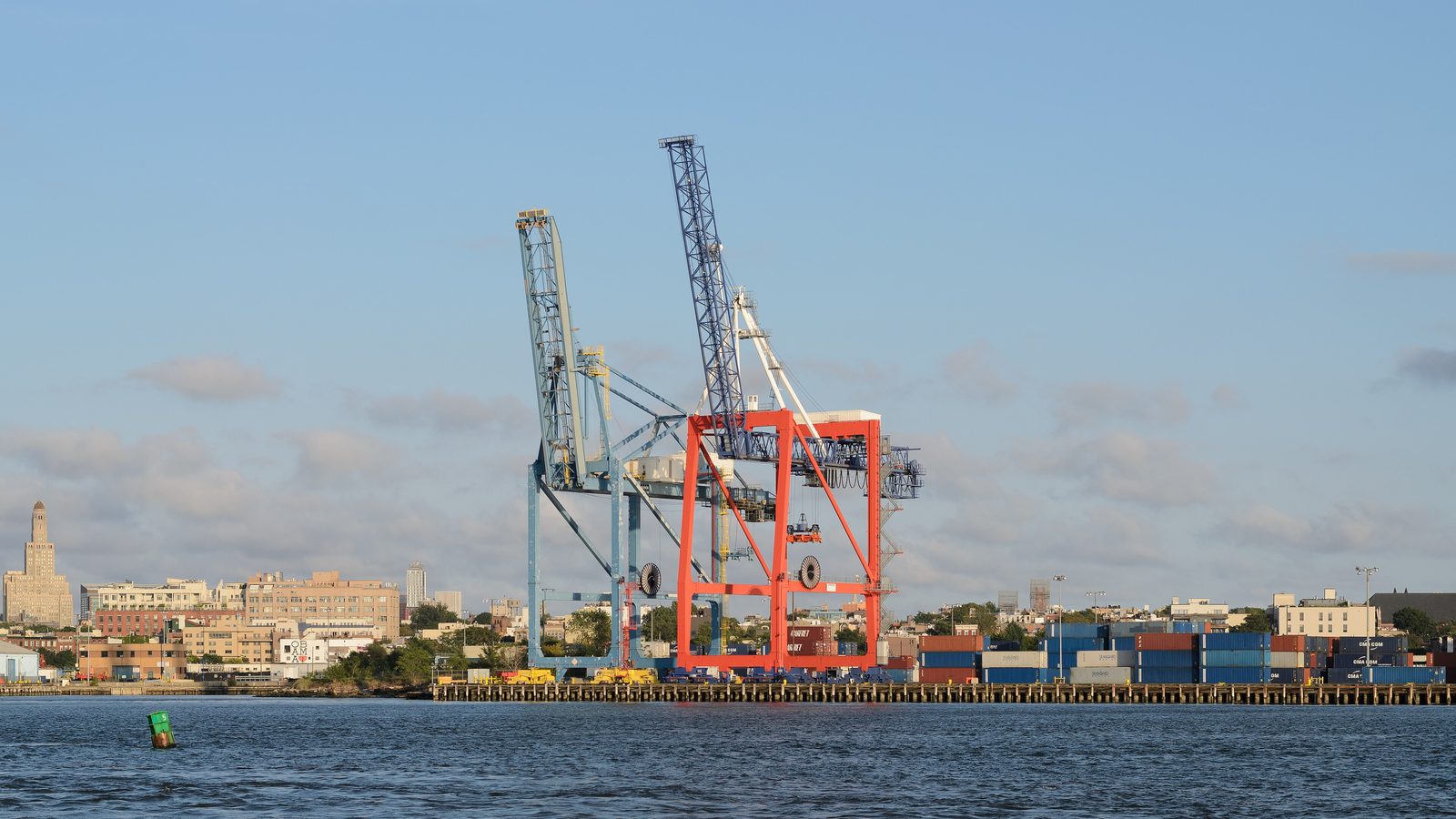 Grues à conteneurs du terminal à conteneurs de Red Hook dans le port de New York, avec des conteneurs empilés et les toits de Brooklyn de l'autre côté de l'eau.