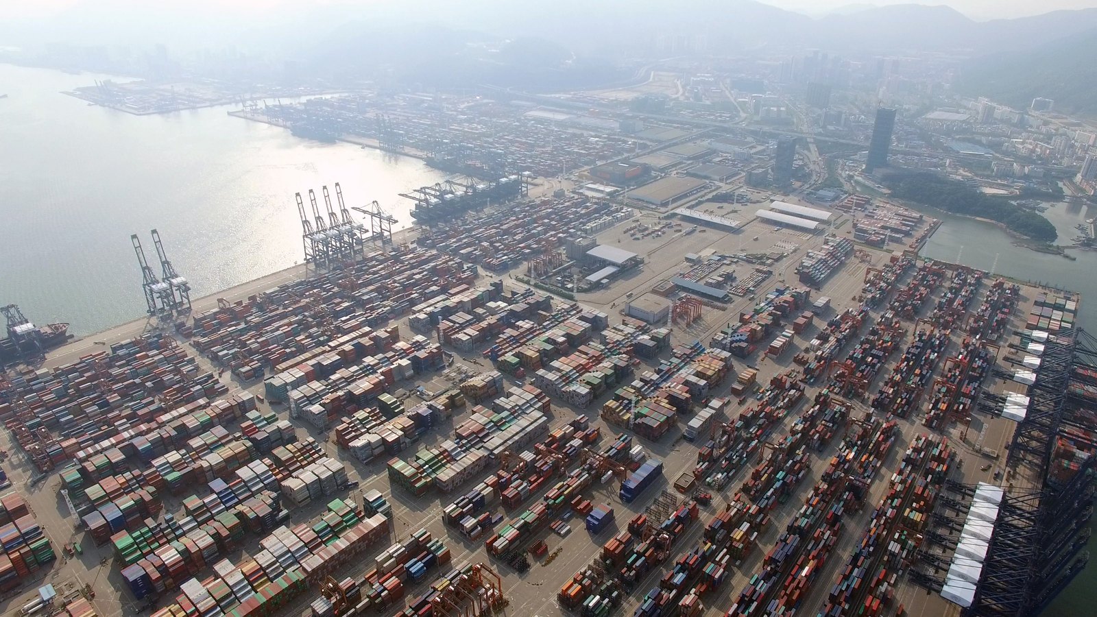 Vue aérienne du terminal à conteneurs international de Yantian à Shenzhen, avec des rangées de conteneurs empilés, des portiques de quai le long du quai et des collines à l'arrière-plan