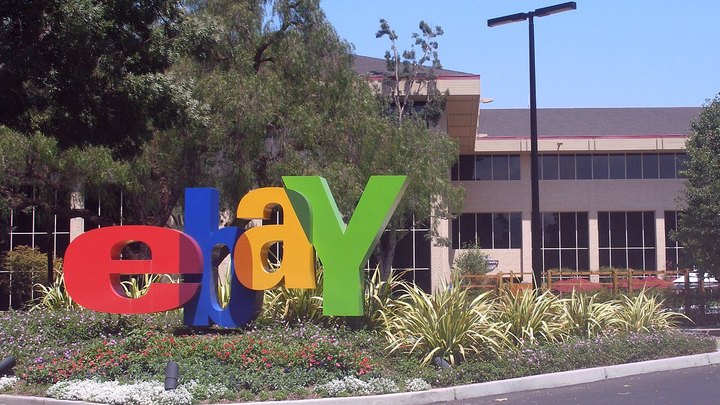 Large red, blue, yellow and green eBay letters in a flower bed in front of a low office building