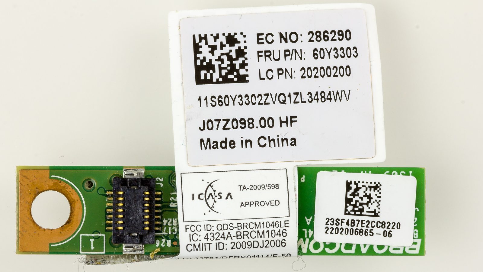 Gros plan d'un petit circuit imprimé vert de module Bluetooth avec une étiquette blanche portant un identifiant FCC, un numéro IC et des codes-barres.