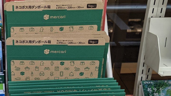 Green Mercari-branded cardboard shipping boxes, printed with their dimensions, stacked on a store display rack