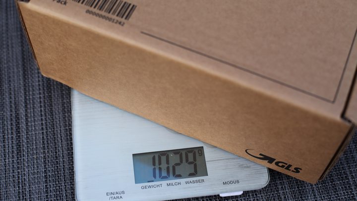 Un carton d'expédition posé sur une balance de cuisine numérique qui affiche 1029 grammes