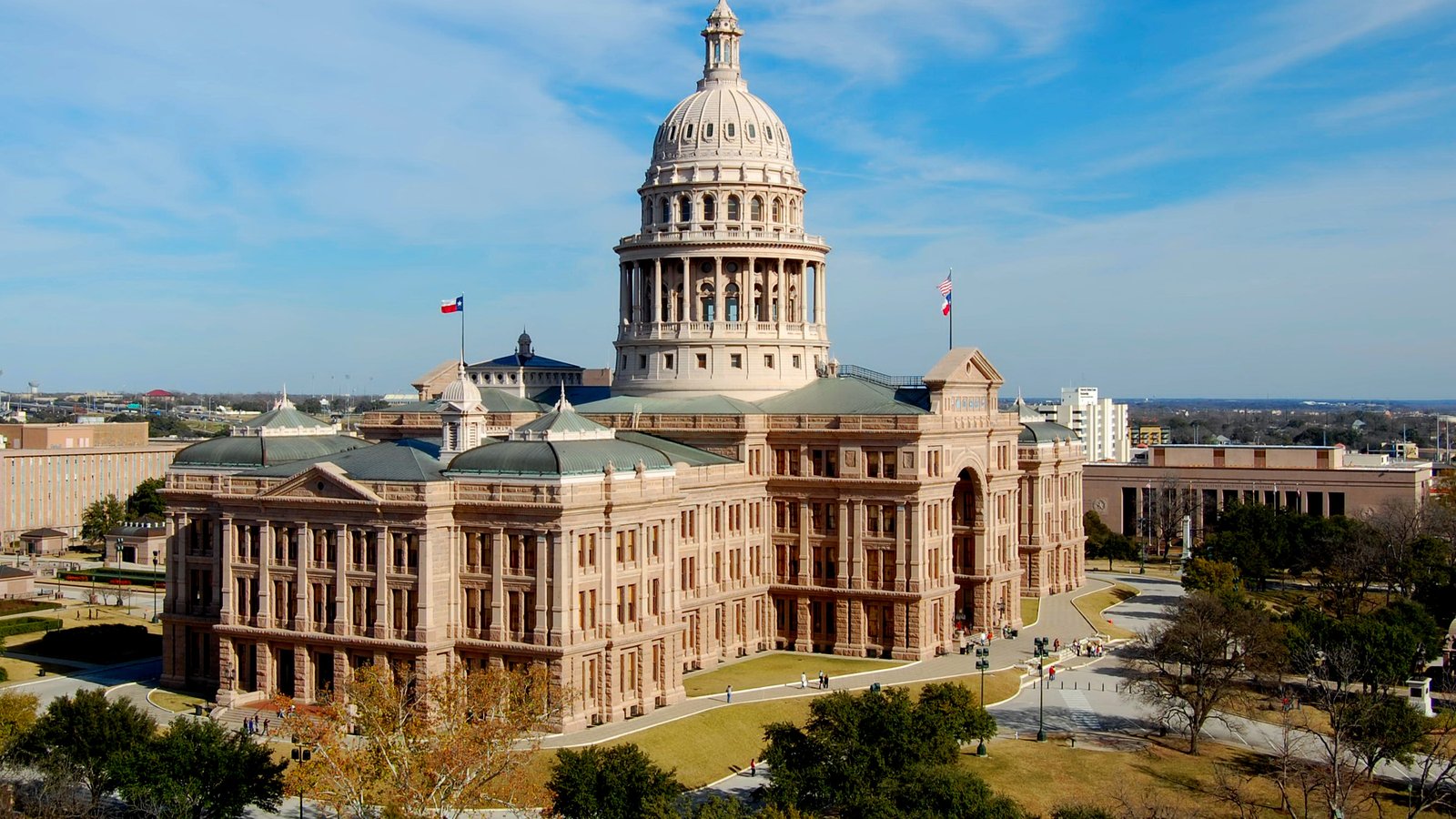 Aerial view of the Texas State Capitol in Austin, a domed granite building with flags, lawns and trees around it