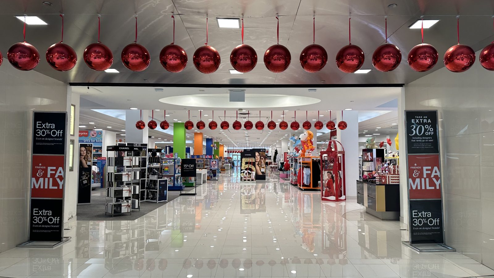Large red ball ornaments hang above the entrance of a department store decorated for Christmas